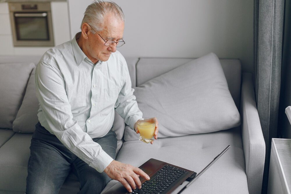 Starszy mężczyzna siedzący na kanapie i posługujący się laptopem